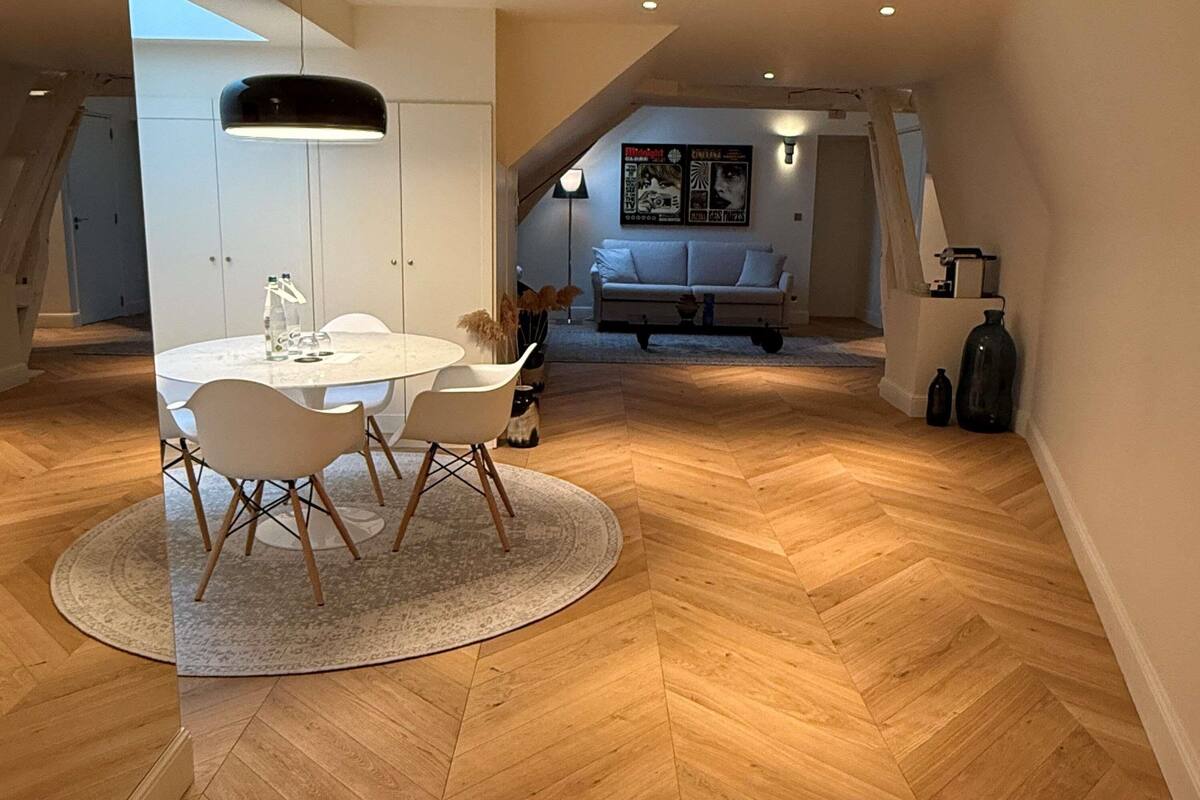 Un espace repas comprenant une table ronde, des chaises et un parquet en bois disposé en motif chevron.