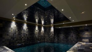 Ein modernes Hallenbad mit dunkel gefliesten Wänden und klarem, blauem Wasser.