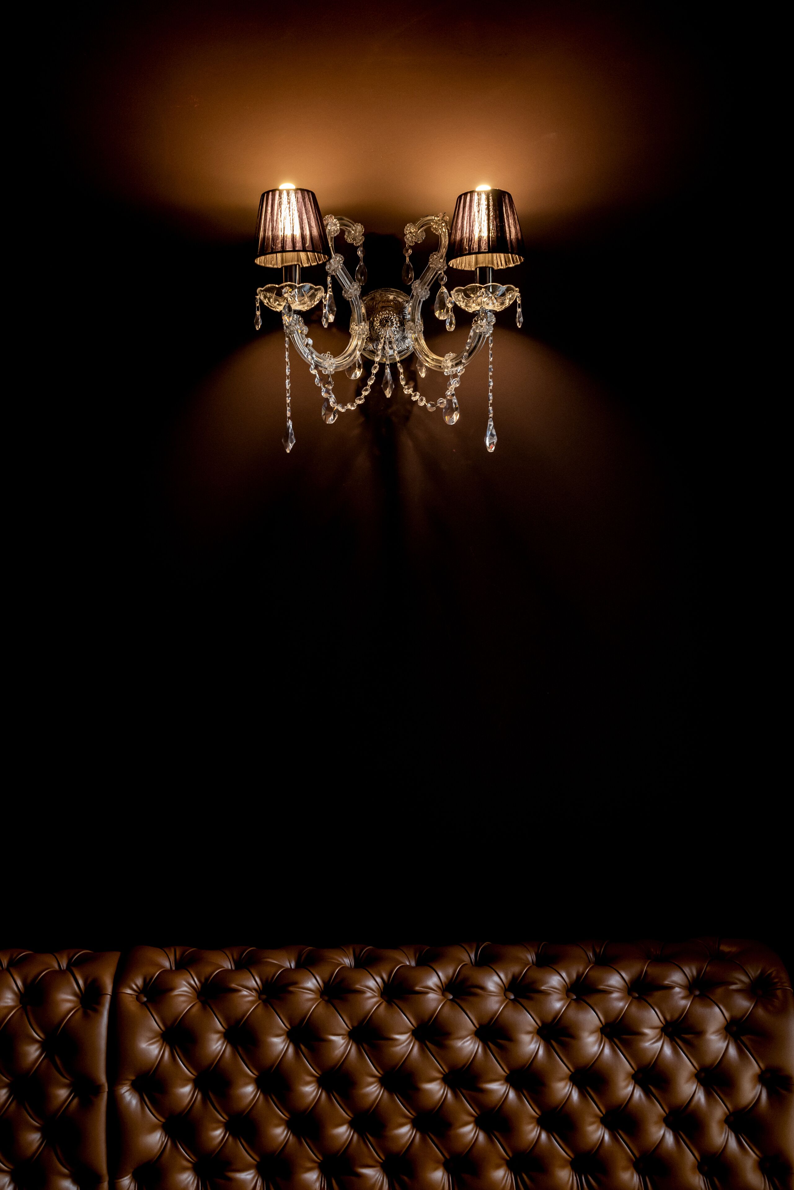A chandelier with two lampshades and a tufted leather sofa.