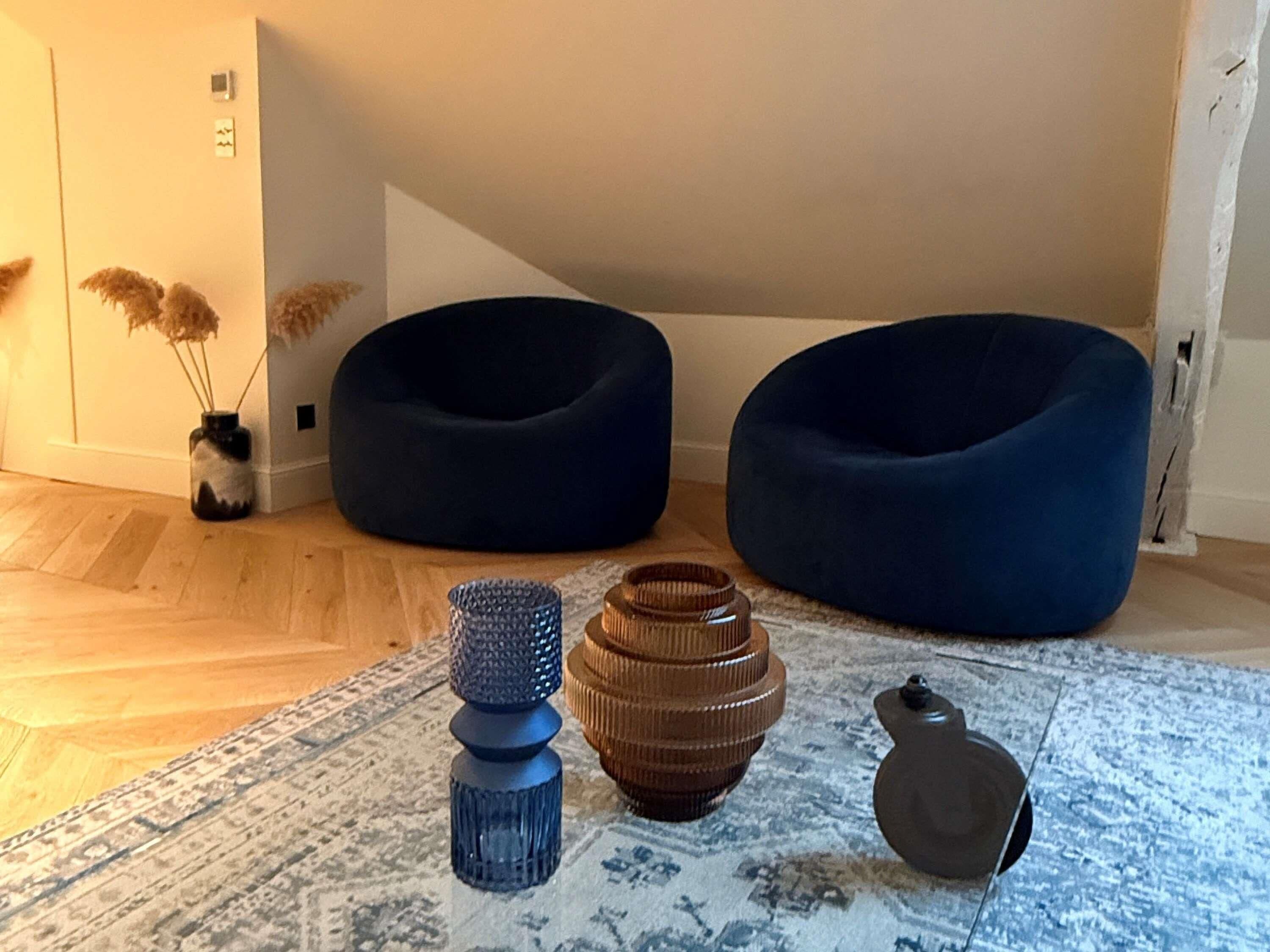 A room with two dark blue bean bags, a patterned rug, and a small vase with dried plants.