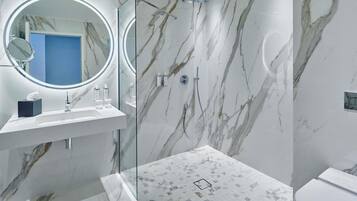 A modern bathroom with a marble wall, a glass shower enclosure, a sink with toiletries, and a toilet.