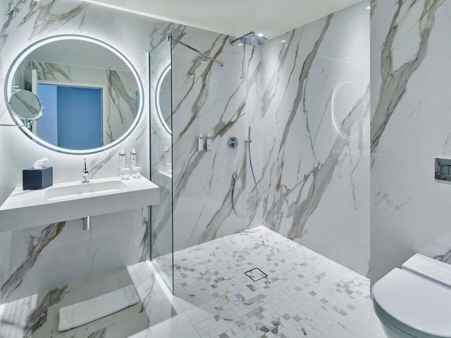 A modern bathroom with a marble wall, a glass shower enclosure, a sink with toiletries, and a toilet.