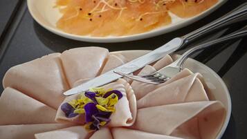 A plate of sliced meat with a garnish of purple and yellow flowers, and another plate with sliced salmon and a lime wedge.