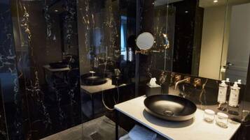Een moderne badkamer met een muur van zwart marmer, een ronde spiegel, een wastafel en een douchehoek.