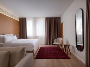 Een hotelkamer met een bed, twee stoelen, een tafeltje, een spiegel en een rood tapijt met een patroon.