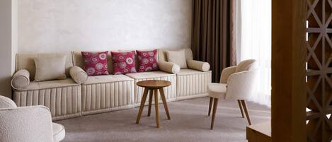 A living room with a sofa, two armchairs, a round coffee table, and a window with curtains.