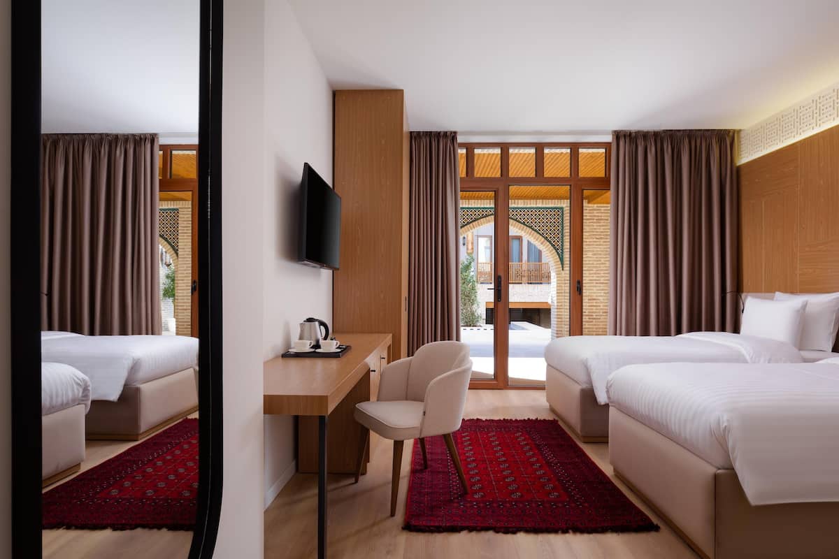 Habitación de hotel con dos camas, un escritorio, una silla, un televisor y vista al exterior.