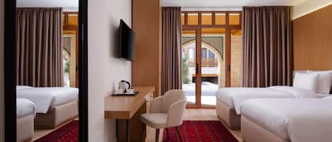 A hotel room with two beds, a desk, a chair, a TV, and a view of the outside.
