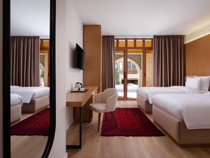 Ein Hotelzimmer mit zwei Betten, einem Schreibtisch, einem Sessel und einem Fernseher, mit Blick ins Freie.