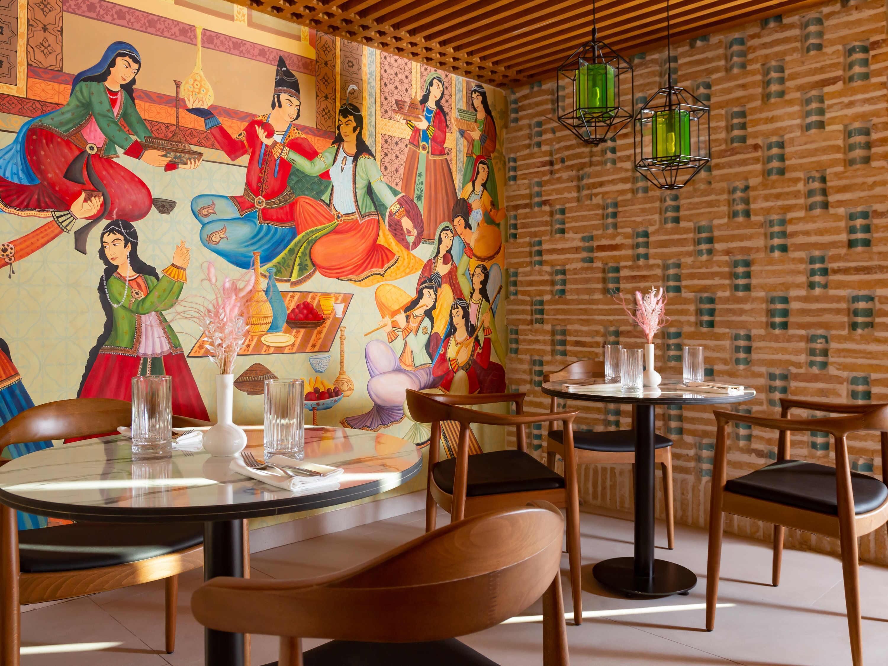 A restaurant with round tables, chairs, and a mural of colorful figures.