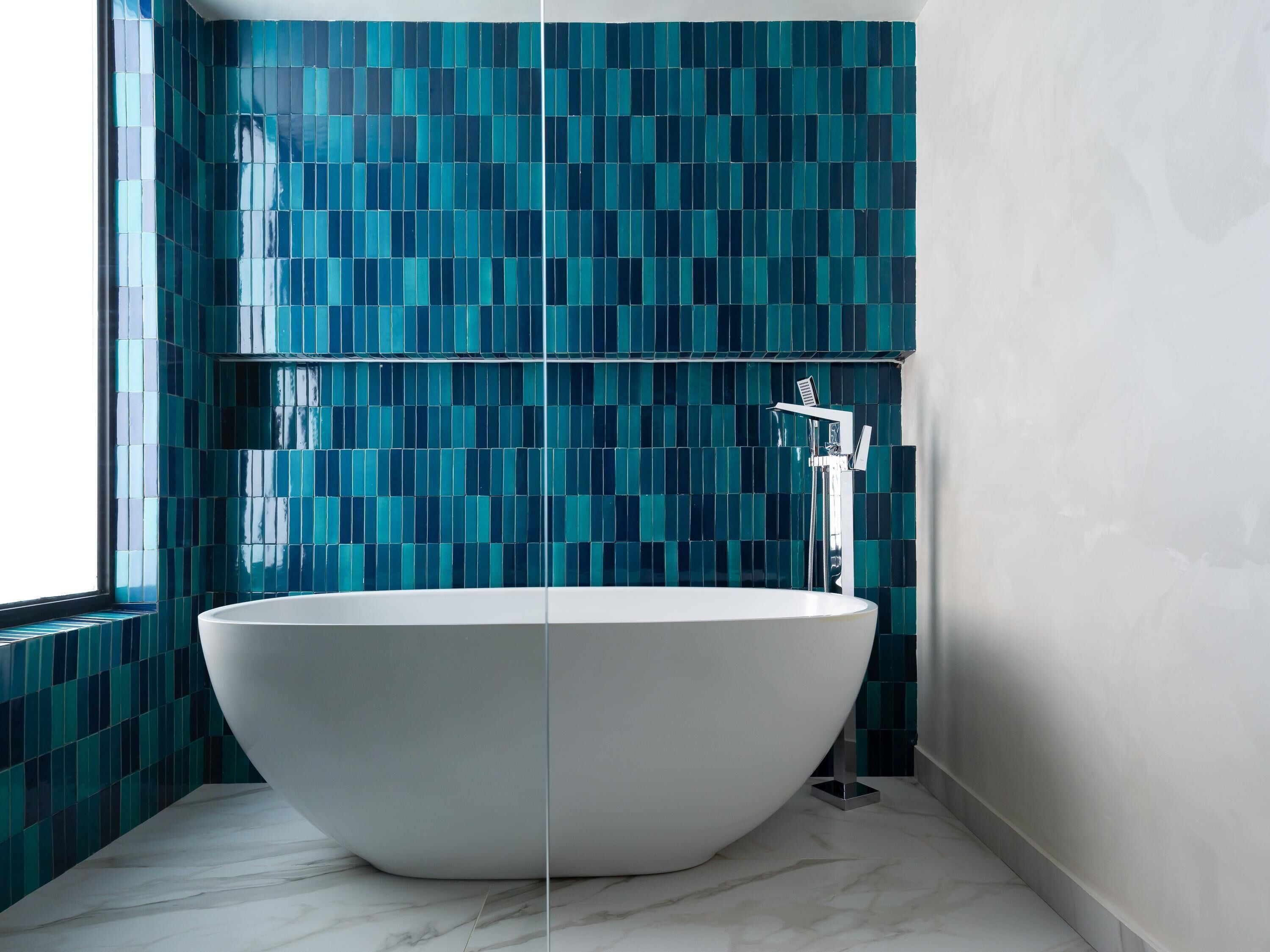 Un baño moderno con una bañera independiente, paredes con azulejos y suelo de mármol.
