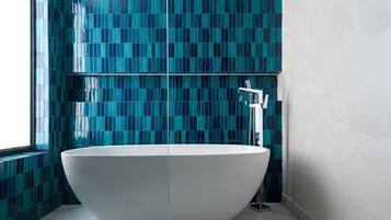 Un baño moderno con una bañera independiente, paredes con azulejos y suelo de mármol.