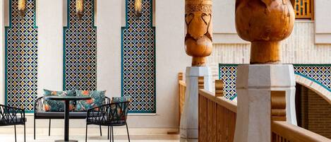 Une cour intérieure aménagée avec un espace salon, des murs décorés de motifs et des colonnes en bois.