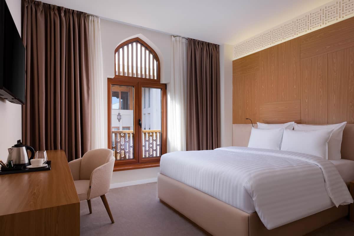 Habitación de hotel con una cama grande, un escritorio con hervidor y taza, y una silla.