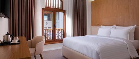 Habitación de hotel con una cama grande, un escritorio con hervidor y taza, y una silla.