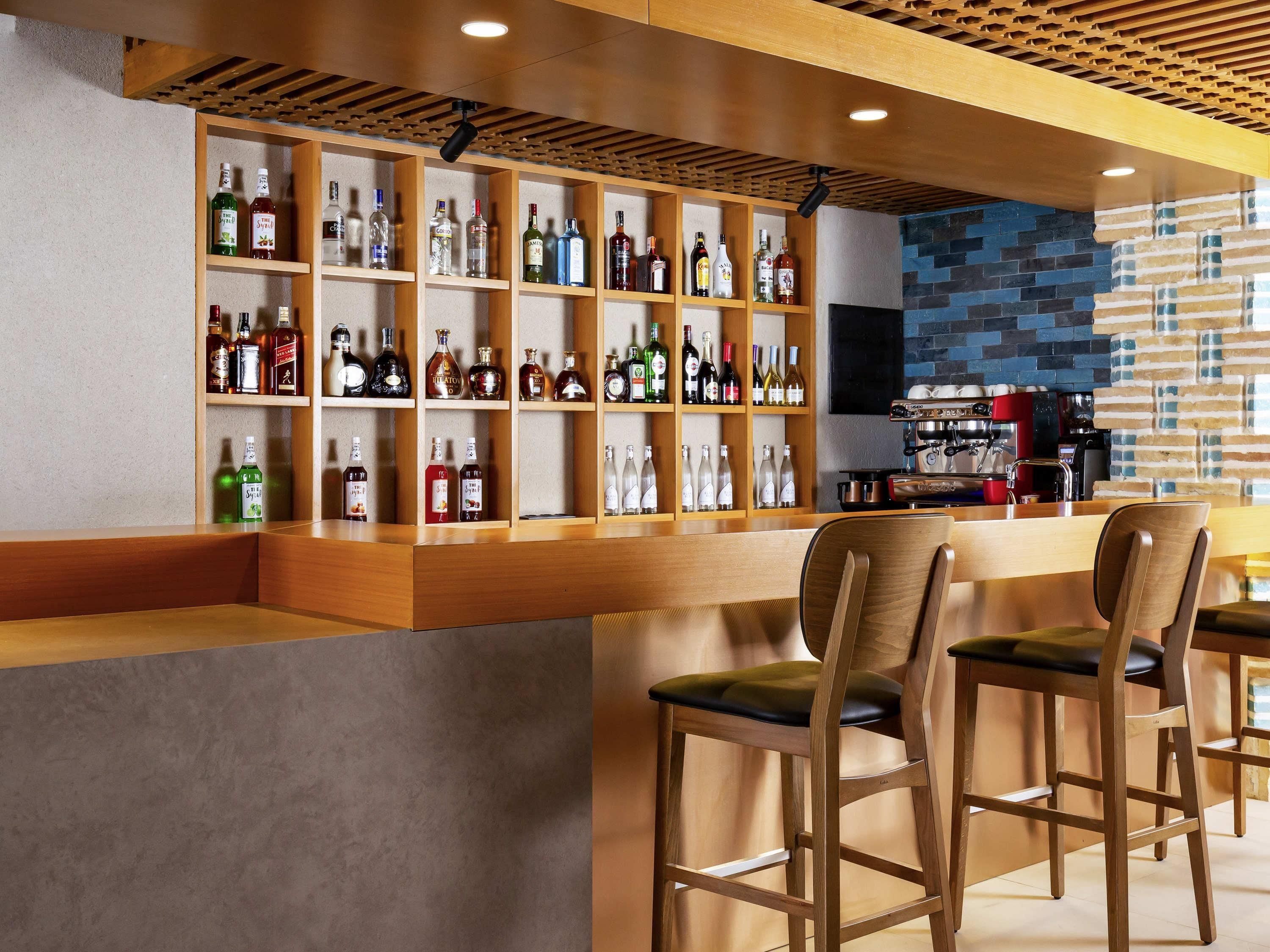 Una zona de bar con estantes de madera llenos de botellas de licores, una barra y taburetes.