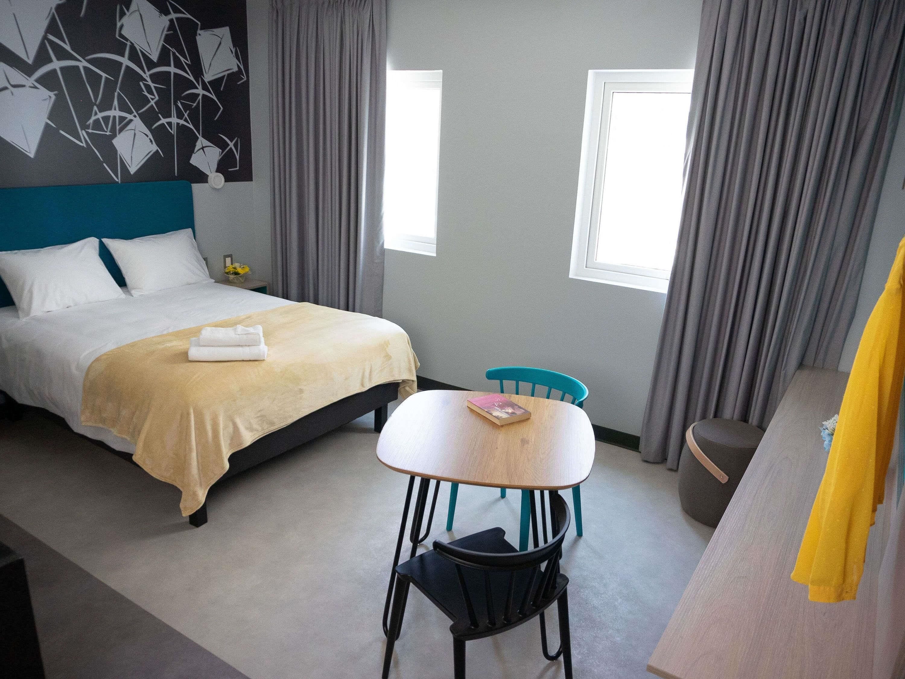 A hotel room with a bed, a table, a chair, a desk, and a window.