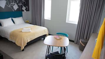 A hotel room with a bed, a table, a chair, a desk, and a window.