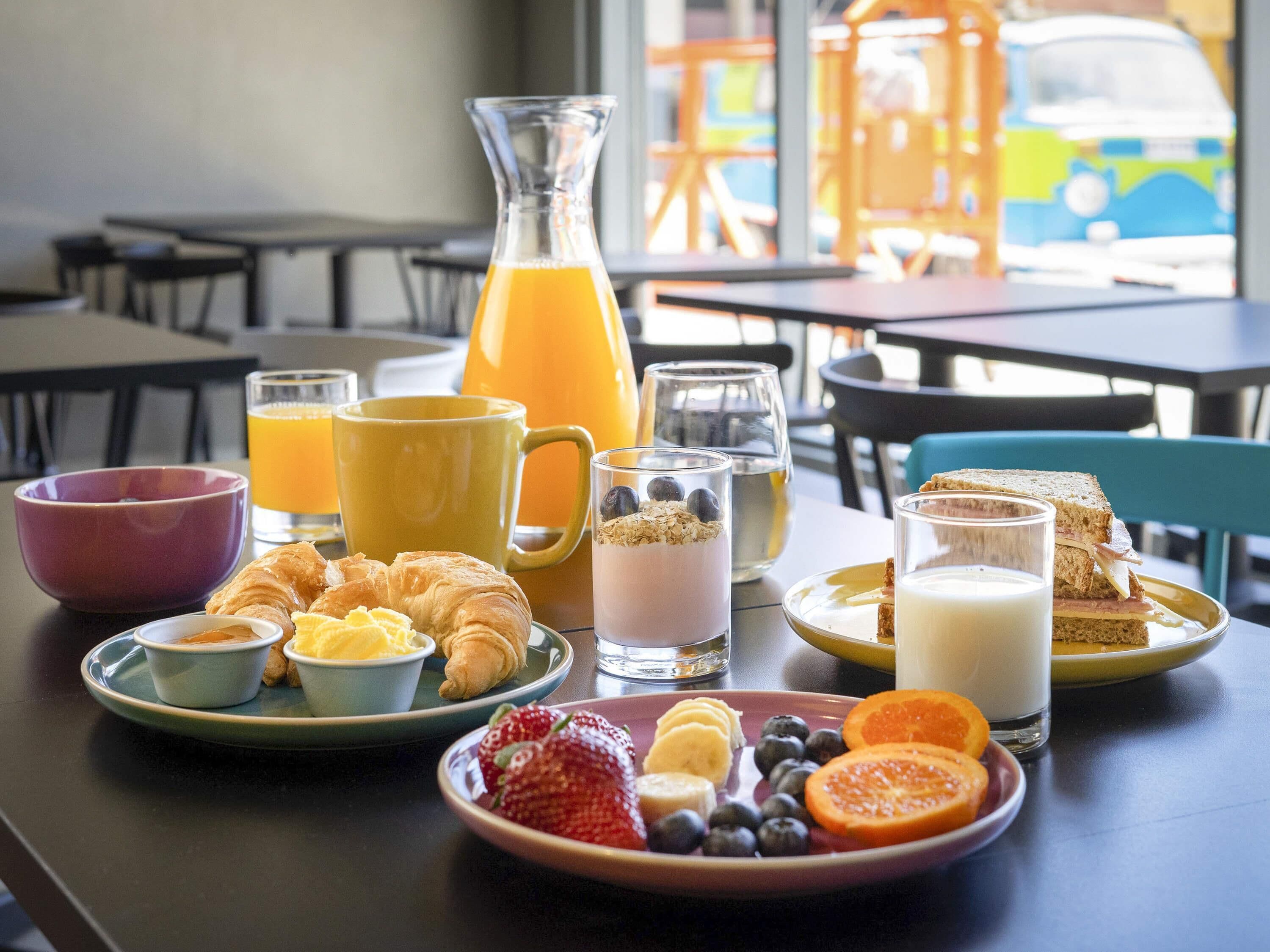 A breakfast table with croissants, fruit, yogurt, and juice.