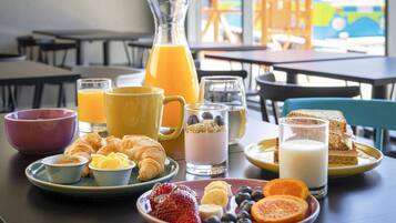 A breakfast table with croissants, fruit, yogurt, and juice.