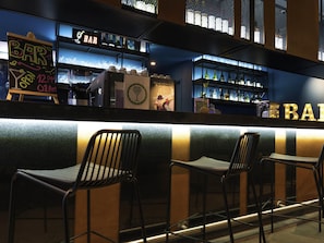 A bar area with a counter, bar stools, and shelves of bottles. - Ibis Styles Antofagasta (Antofagasta)