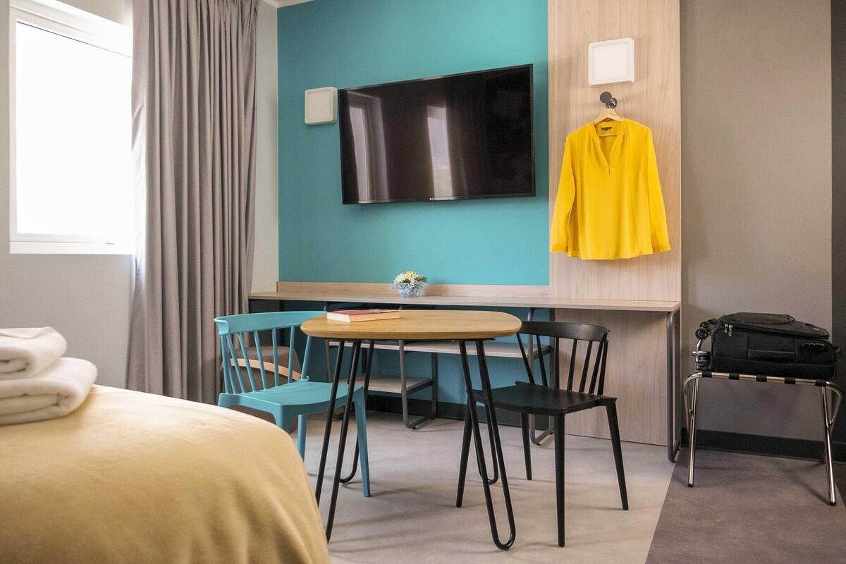 Habitación de hotel con cama, escritorio, televisor, silla y maleta.