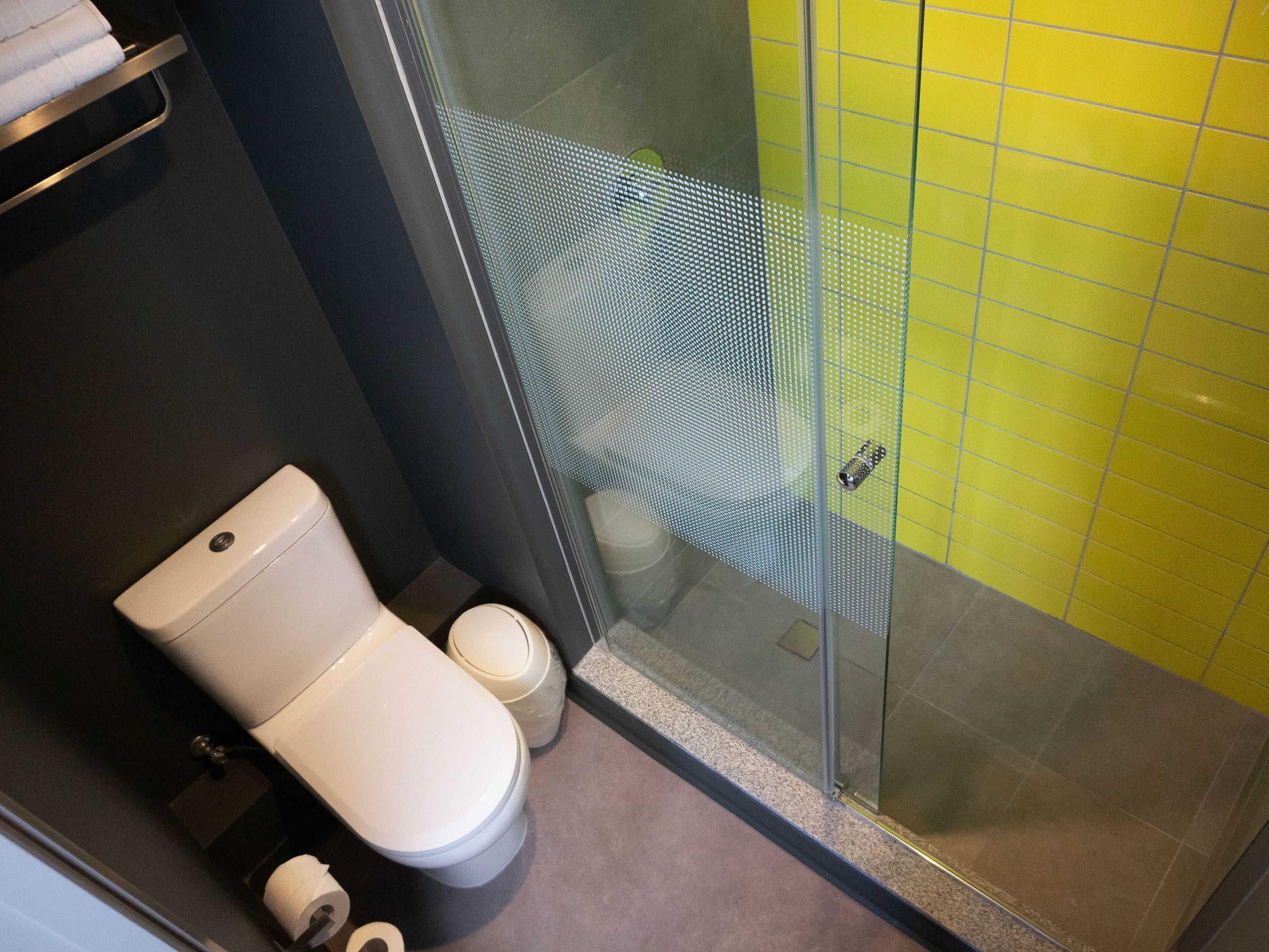 A bathroom with a toilet, a glass shower enclosure, and a yellow tiled wall.