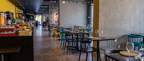 A restaurant interior with high ceilings, exposed ductwork, and a mix of modern and industrial decor. Tables are set with wine glasses and plates, and a Christmas tree is visible in the background.