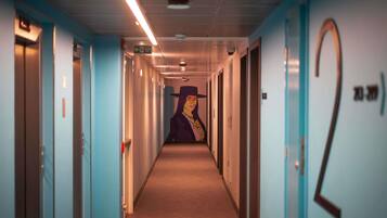 Un pasillo con puertas numeradas 2 y 3, un corredor con piso alfombrado y una pared con un mural.