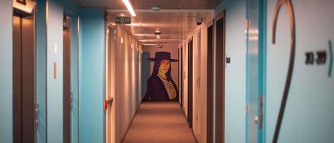 Un pasillo con puertas numeradas 2 y 3, un corredor con piso alfombrado y una pared con un mural.