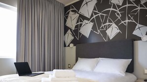 A hotel room with a bed, a laptop on the bed, and a wall with abstract art. - Ibis Styles Antofagasta (Antofagasta)
