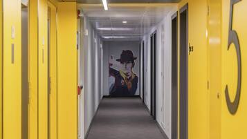 Un pasillo con puertas amarillas, un letrero con el número 5 y un mural de un hombre con sombrero.