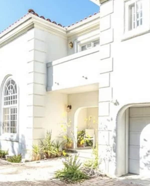 A white building with a large arched window, a garage door, and a small garden area with plants.