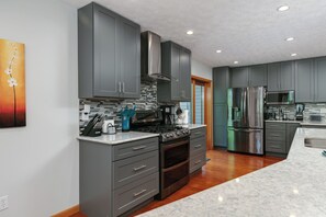 A modern kitchen with grey cabinets, a stainless steel range, and a large island with a microwave. - Watkins Glen, Corning, Finger Lakes 3 BR 3 Bath w/ Hot Tub (Campbell)