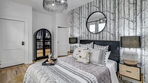 A bedroom with a large bed, a round mirror, a black headboard, and a side table with a lamp. - Forth House – Stylish & Cozy 1 BR Apt in Springfield (Jacksonville)