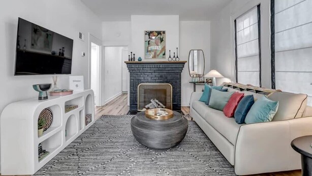 A modern living room with a fireplace, a sofa with colorful cushions, a flat-screen TV, and a decorative coffee table. - Forth House – Stylish & Cozy 1 BR Apt in Springfield (Jacksonville)