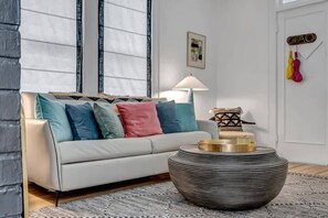 Una sala de estar moderna con un sofá blanco, cojines coloridos, una mesa redonda de centro y una lámpara.