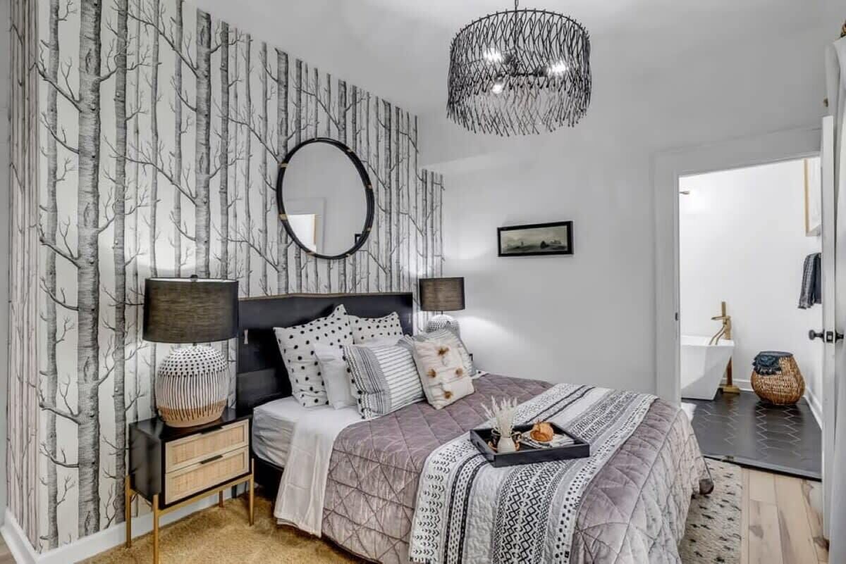 A bedroom with a bed, bedside tables, a mirror, and a wall with a tree pattern.