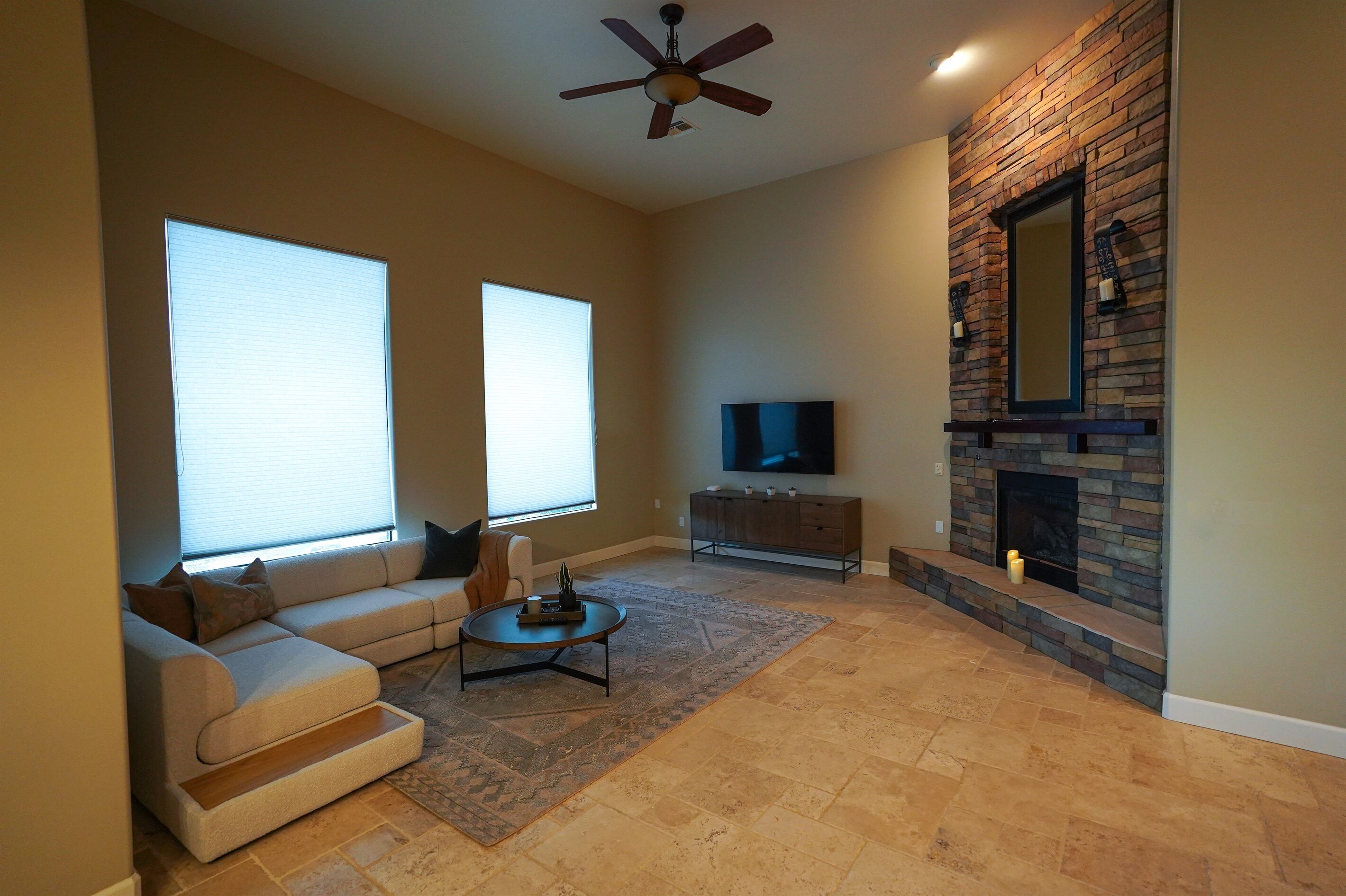 A living room with a sofa, coffee table, fireplace, TV, and a ceiling fan.