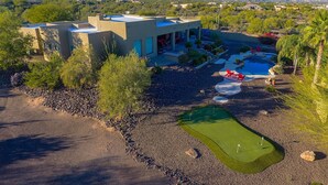 Ein modernes Haus mit Swimmingpool, einer Terrasse mit roten Stühlen und einem Golfplatz.
