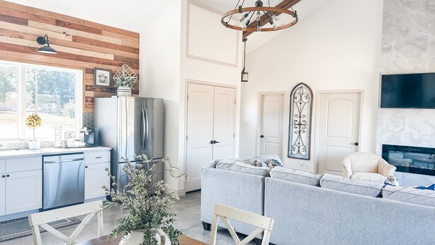 A modern kitchen with a built-in refrigerator, a dining table with a vase, and a grey sofa in a living area with a fireplace.