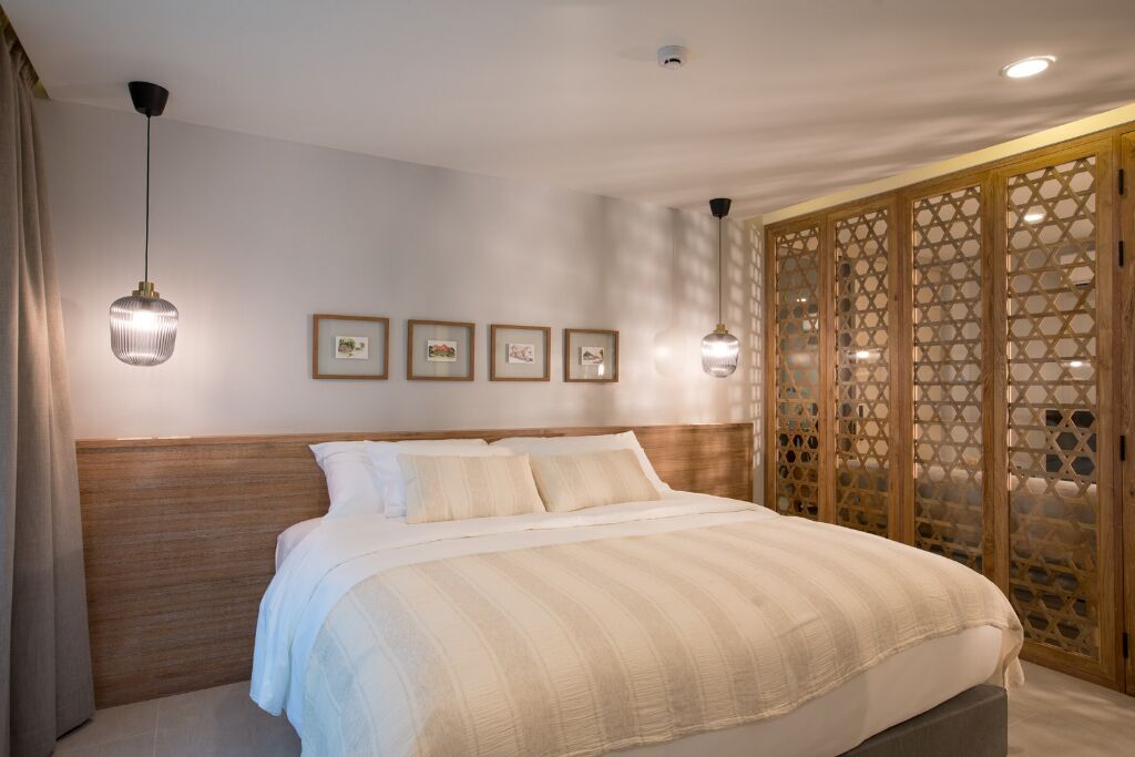 Un lit bien fait, avec une tête de lit en bois, un ensemble de tableaux encadrés accrochés au mur et une cloison en treillis de bois.