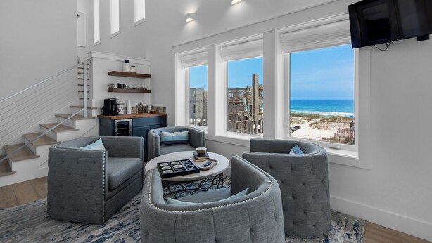 Ein geräumiges Wohnzimmer mit Blick auf den Strand, ein Küchenbereich mit Holzregalen und eine Treppe.