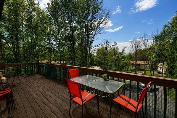 A wooden deck with a table and chairs, surrounded by a metal railing, overlooking a residential area.