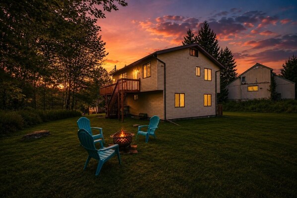 A two-story house with a deck and a fire pit in the yard.