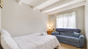 Un dormitorio con cama, sofá, mesita de noche con lámpara y ventana con cortinas.