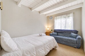 A bedroom with a bed, a sofa, a bedside table with a lamp, and a window with curtains. - Walk to Beach, Spacious Backyard (Lake Ariel)