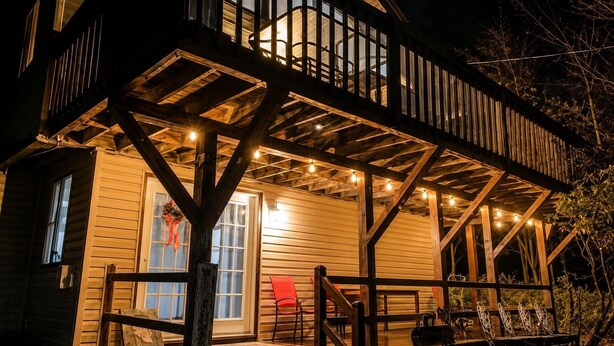 Una cabaña de madera con terraza, porche cubierto y luces colgantes.