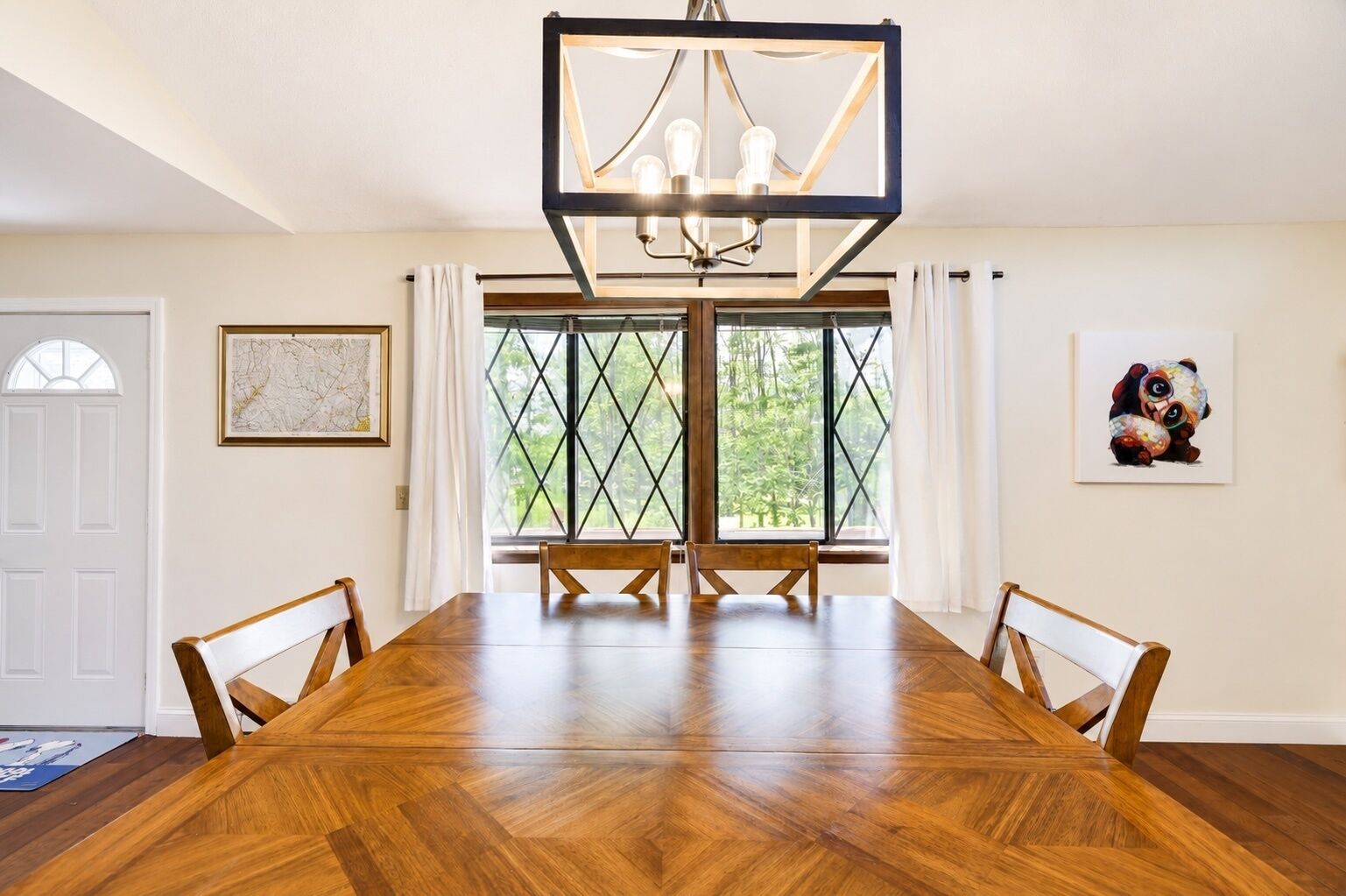 Comedor con una amplia mesa de madera, sillas, una araña y una ventana con vista a árboles.