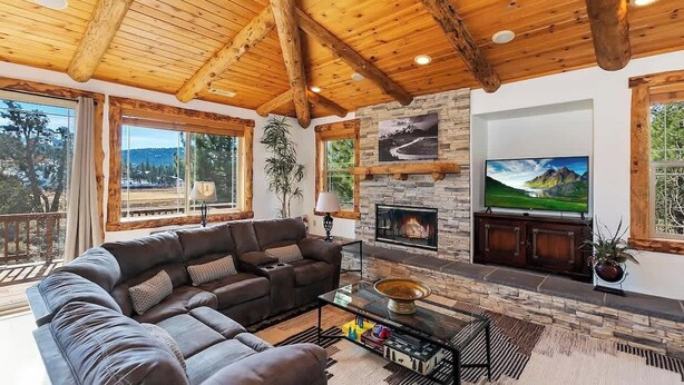 Una sala acogedora con chimenea de piedra, vigas de madera en el techo y amplias ventanas con vistas panorámicas.